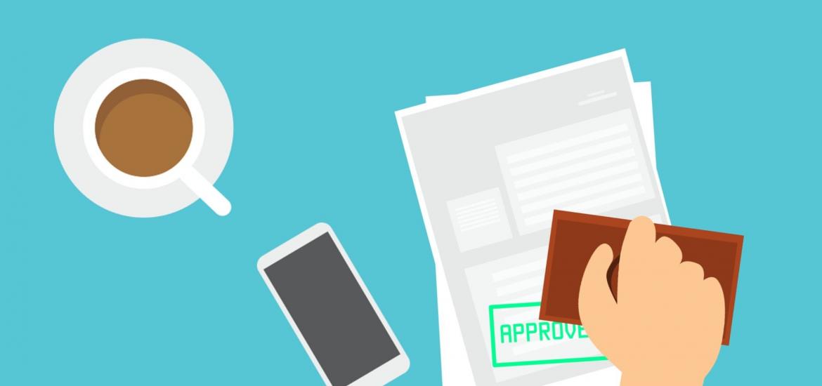 hand holding approved stamp over paper with coffee and phone lying on table next to the paper. There's a lot going on here, seriaouly. 