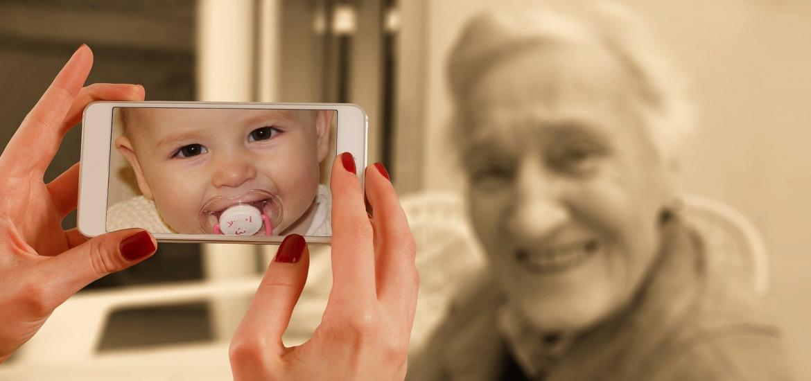 old woman in background with picture of a baby in the forefront on a cell phone